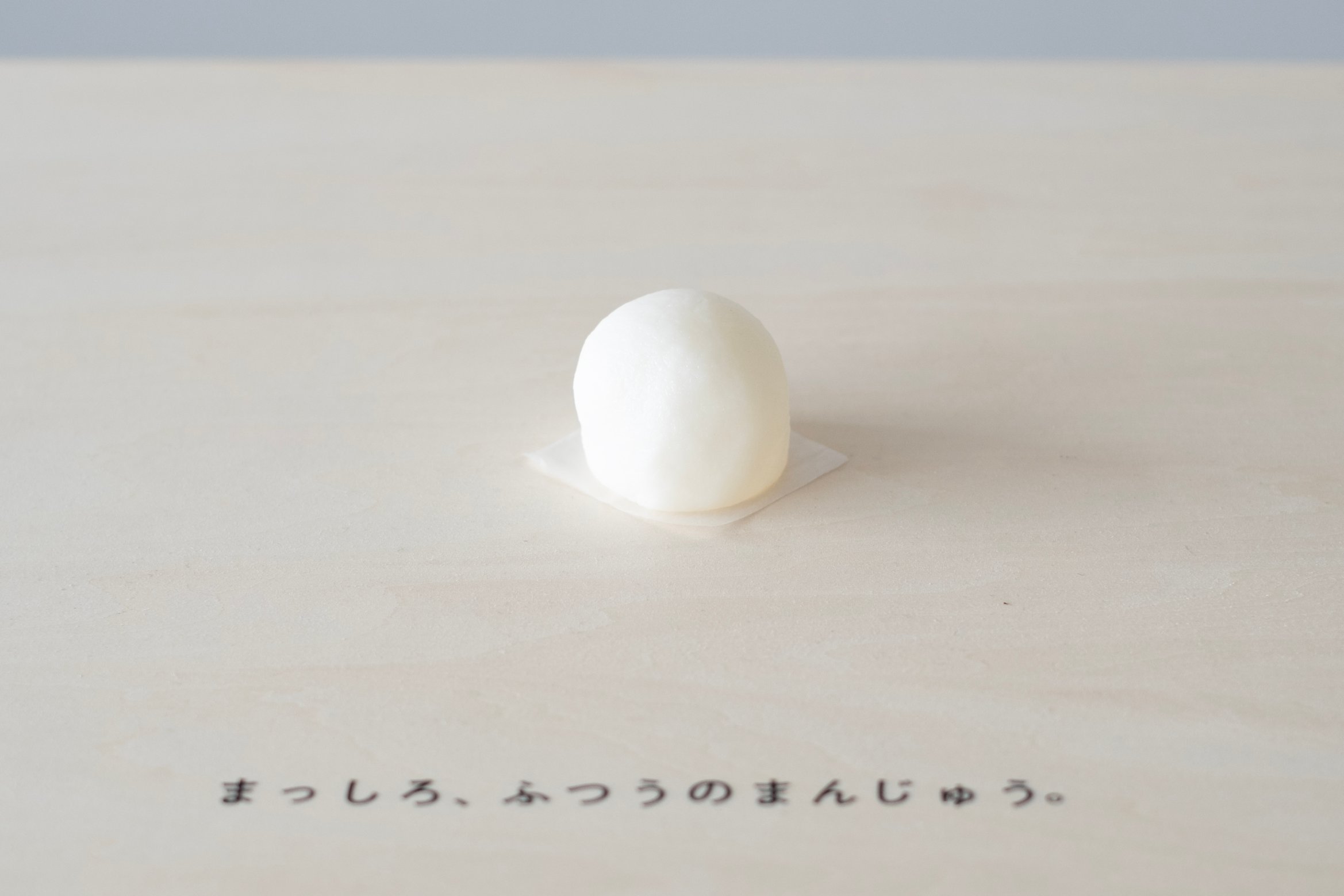 まんじゅうが展示台の上に置かれている。「まっしろ、ふつうのまんじゅう」と台の上に書かれている。